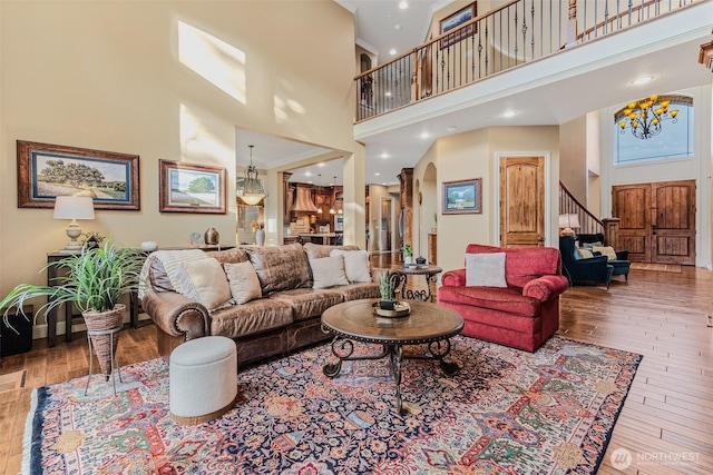 living area with arched walkways, a towering ceiling, an inviting chandelier, and hardwood / wood-style flooring