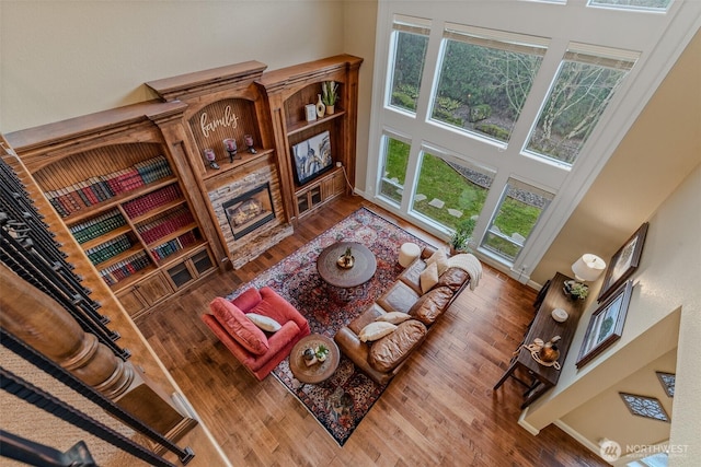 living room featuring a stone fireplace, wood finished floors, a high ceiling, and baseboards