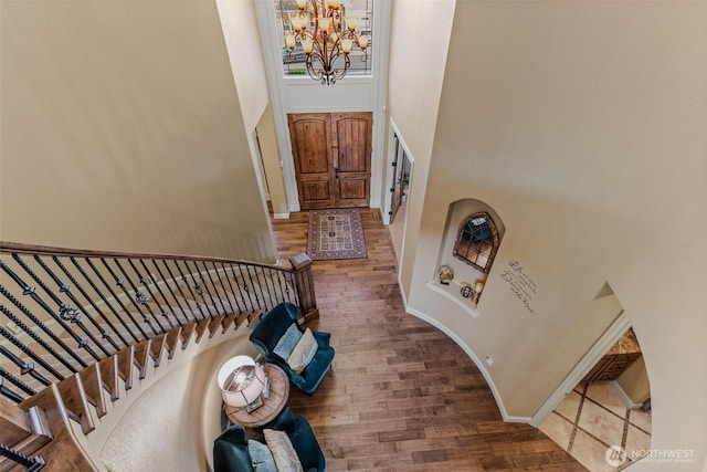 foyer featuring baseboards, a towering ceiling, wood finished floors, an inviting chandelier, and stairs