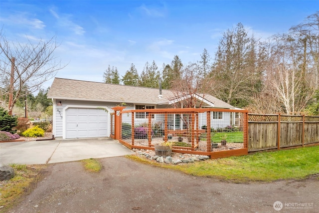 ranch-style home featuring fence, concrete driveway, roof with shingles, a garden, and an attached garage