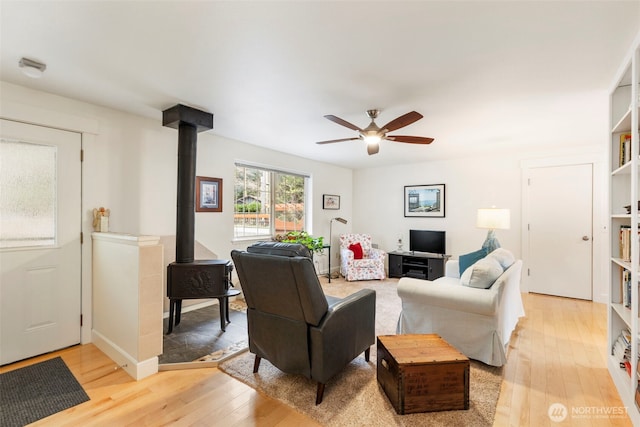 living area featuring a wood stove, a ceiling fan, and light wood finished floors