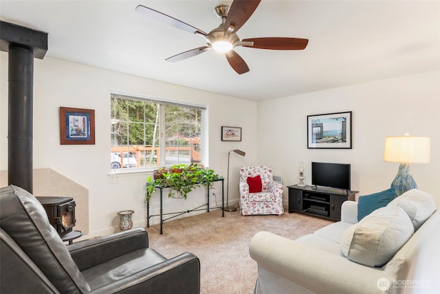 living room featuring a wood stove, a ceiling fan, and carpet floors