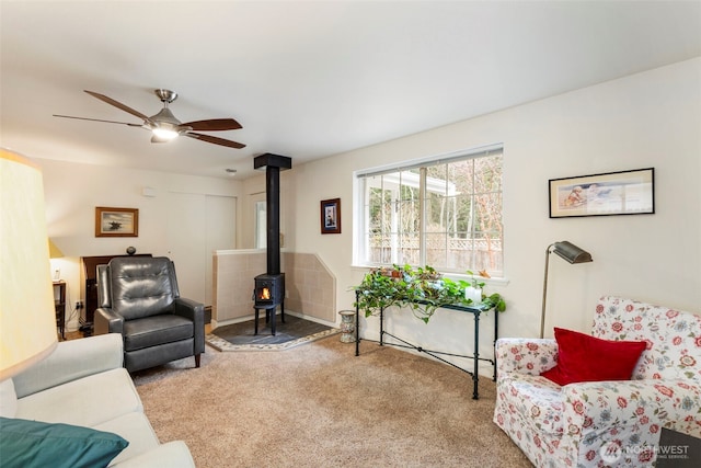 carpeted living room featuring a wood stove and ceiling fan