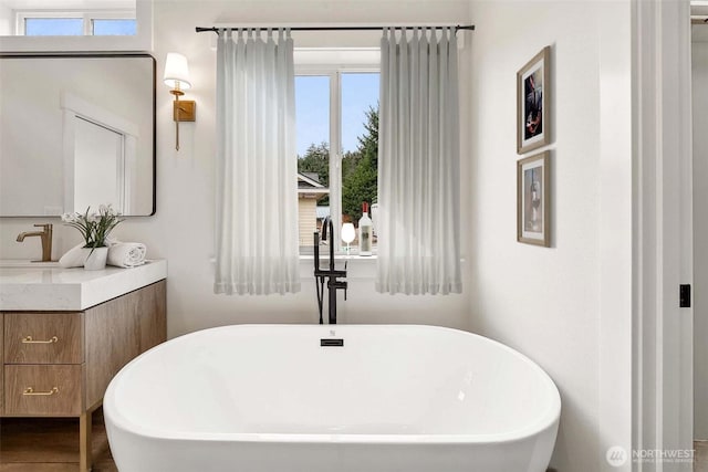 full bath with a freestanding bath, vanity, and wood finished floors