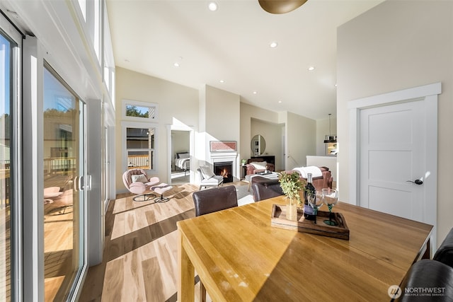 dining area featuring a healthy amount of sunlight, a warm lit fireplace, wood finished floors, and recessed lighting