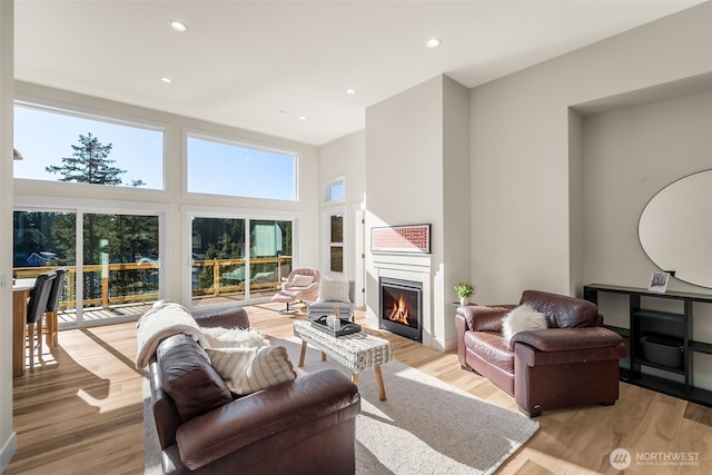 living room with light wood-type flooring, a glass covered fireplace, a high ceiling, and recessed lighting