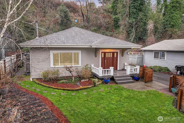 view of front of home with a patio area, roof with shingles, a front lawn, and fence