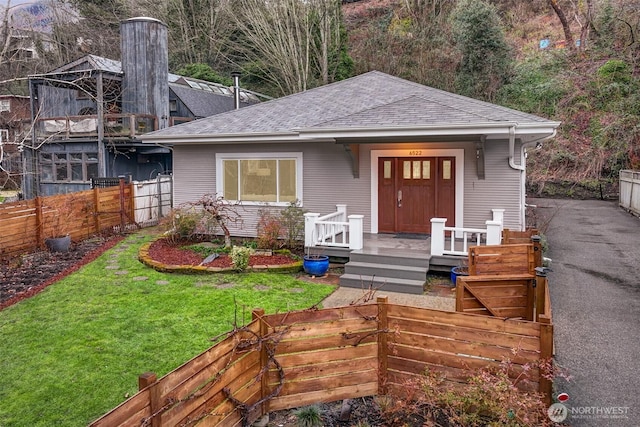 view of front of home with a porch, fence, a front lawn, and roof with shingles