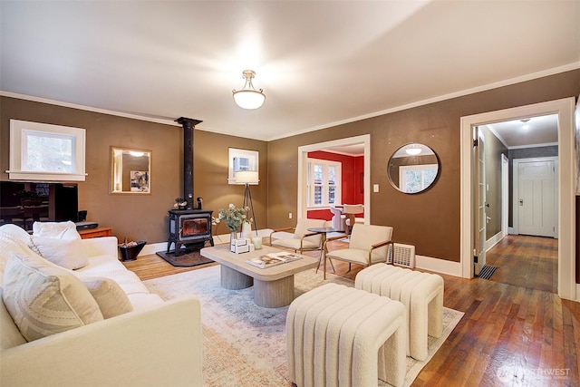 living area with baseboards, wood finished floors, a wood stove, and ornamental molding