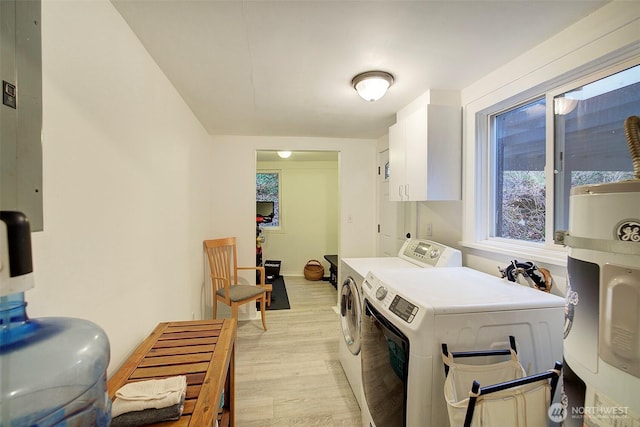 clothes washing area with water heater, washing machine and dryer, light wood-style flooring, and baseboards