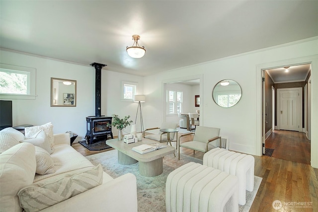 living area featuring baseboards, ornamental molding, wood finished floors, and a wood stove