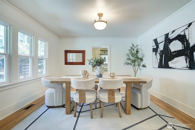 dining area with baseboards, visible vents, ornamental molding, and light wood-type flooring