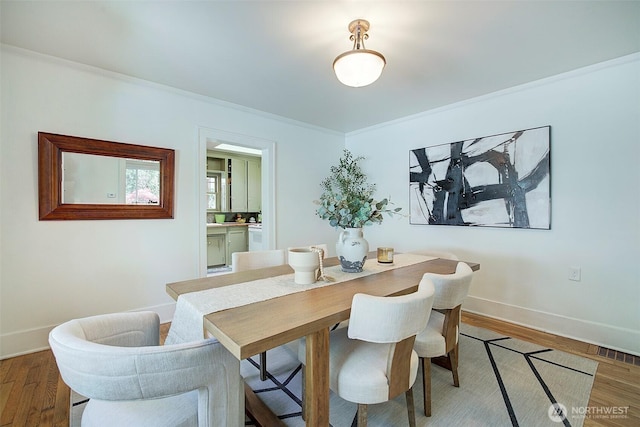 dining space featuring baseboards, visible vents, ornamental molding, and wood finished floors