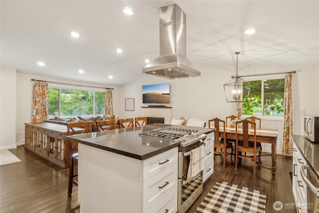 kitchen featuring island range hood, dark wood finished floors, a kitchen breakfast bar, stainless steel appliances, and a fireplace