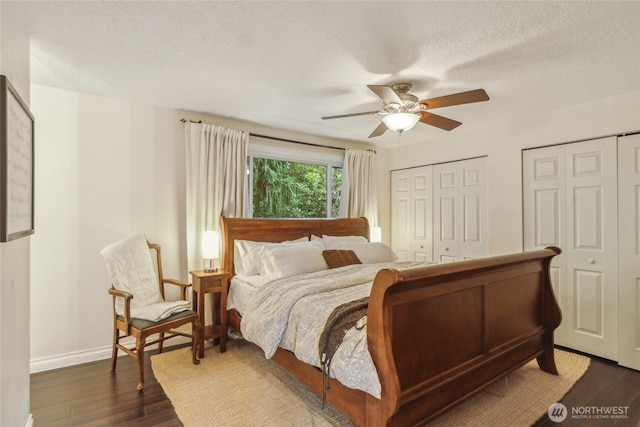 bedroom with a textured ceiling, a ceiling fan, baseboards, multiple closets, and dark wood-style floors