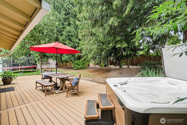 wooden deck featuring a trampoline, outdoor dining area, a fenced backyard, and a hot tub