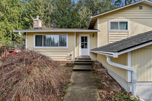 view of front facade featuring entry steps, a shingled roof, and a chimney