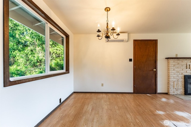 interior space featuring a wall unit AC, a fireplace, light wood-style flooring, a chandelier, and baseboards