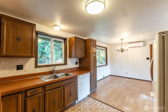 kitchen featuring brown cabinets, hanging light fixtures, a wall mounted AC, a sink, and white appliances