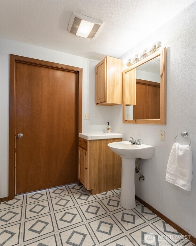 bathroom featuring a sink, baseboards, a textured ceiling, and tile patterned floors