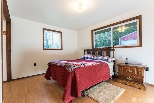 bedroom featuring a baseboard heating unit, baseboards, and wood finished floors