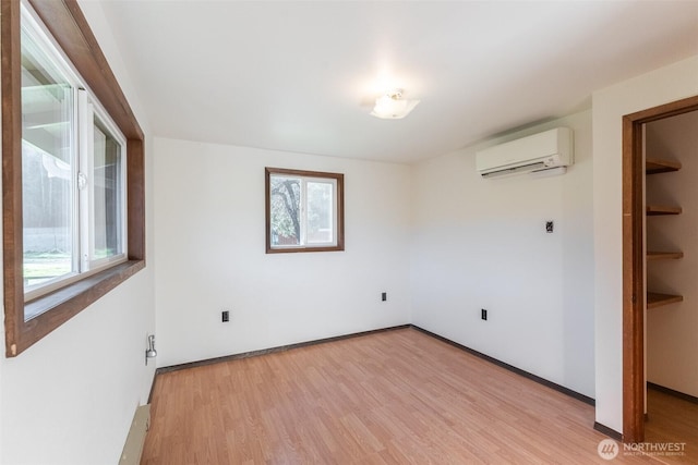 unfurnished bedroom featuring light wood-style floors, an AC wall unit, multiple windows, and baseboards