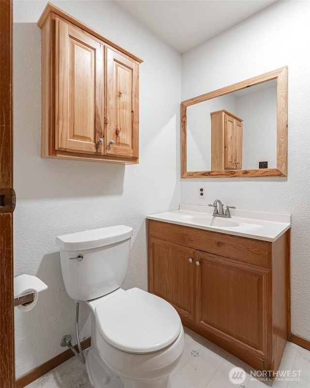 half bathroom with baseboards, vanity, and toilet