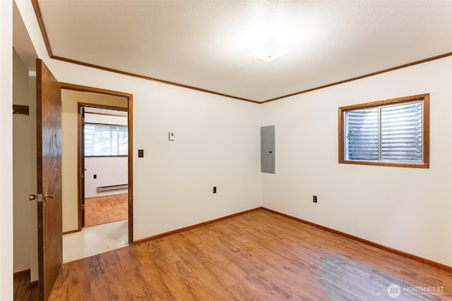 spare room featuring electric panel, baseboards, light wood-style flooring, ornamental molding, and baseboard heating