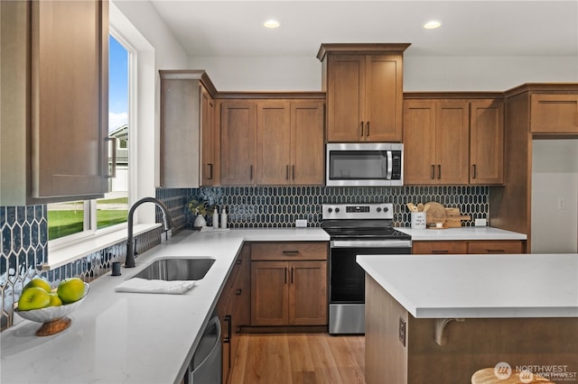 kitchen with light wood finished floors, appliances with stainless steel finishes, backsplash, and a sink