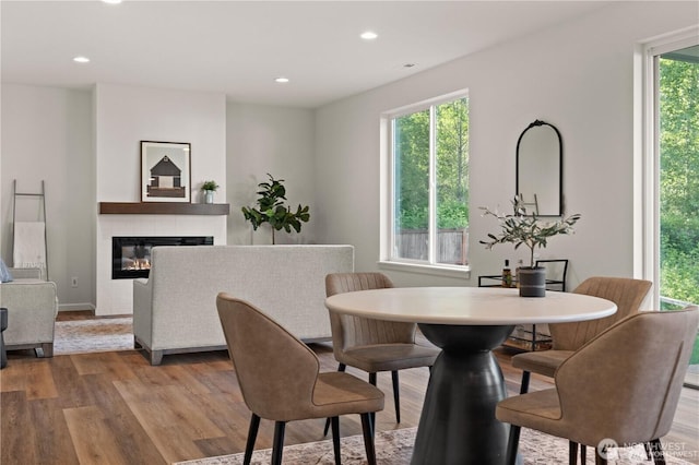 dining space with recessed lighting, a tiled fireplace, light wood-style flooring, and a healthy amount of sunlight