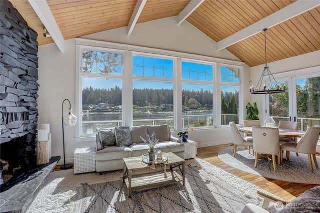 sunroom featuring a fireplace, a water view, lofted ceiling with beams, a wooded view, and a chandelier