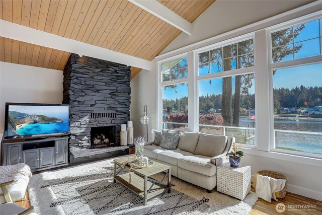 interior space with baseboards, lofted ceiling with beams, wood finished floors, a water view, and a stone fireplace