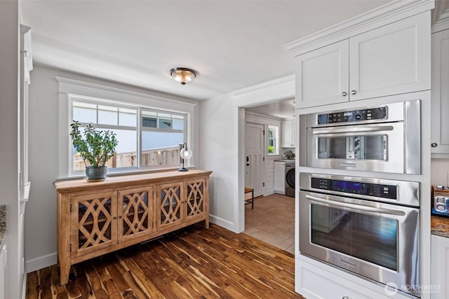 kitchen featuring double oven, stone countertops, dark wood-style flooring, white cabinets, and washer / clothes dryer