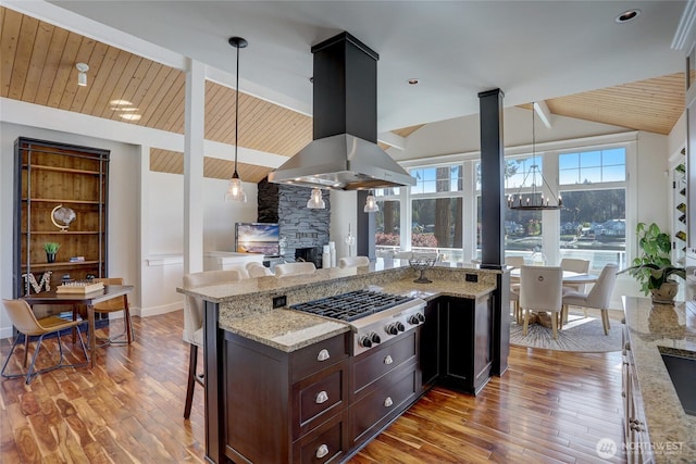 kitchen featuring light stone counters, a fireplace, a kitchen breakfast bar, hanging light fixtures, and island exhaust hood