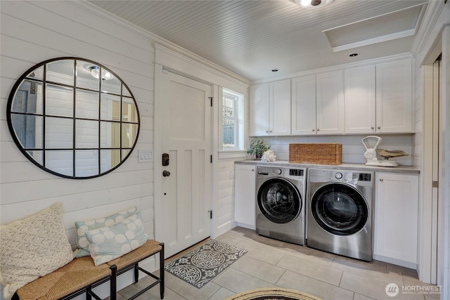 washroom with cabinet space, washing machine and dryer, light tile patterned floors, and wood walls