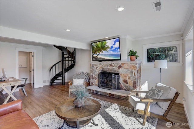 living area featuring crown molding, a stone fireplace, wood finished floors, baseboards, and stairs