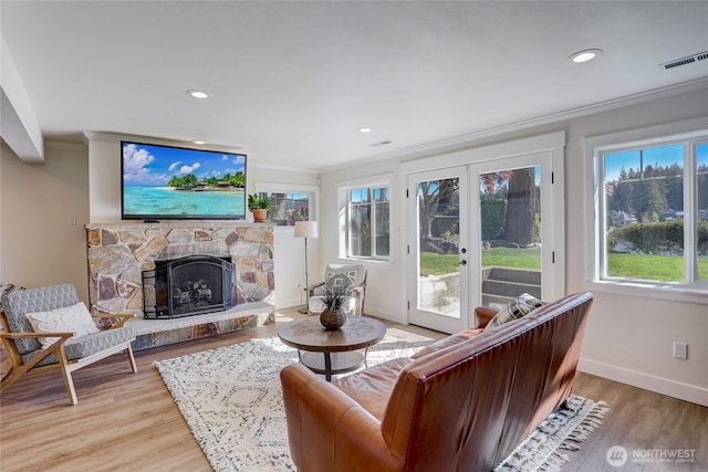 living room featuring light wood-type flooring, a fireplace, visible vents, and crown molding