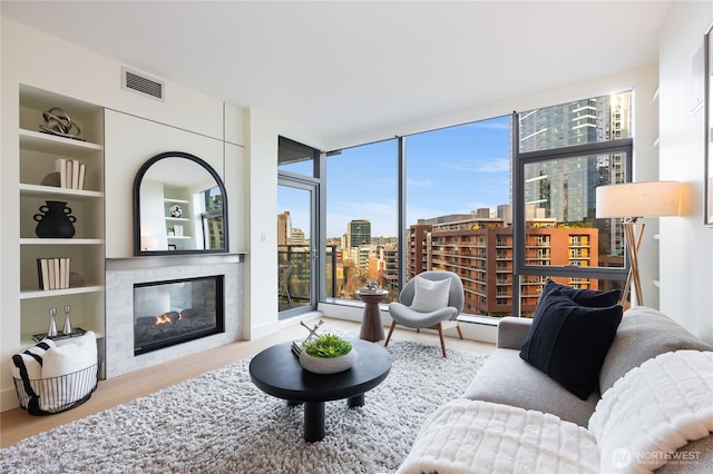 living room featuring floor to ceiling windows, a city view, visible vents, a tiled fireplace, and wood finished floors