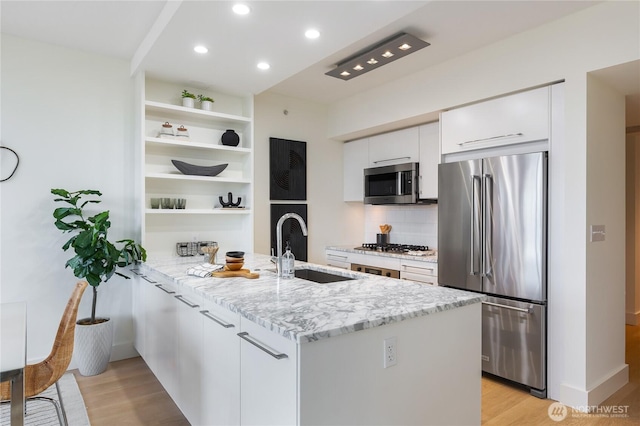 kitchen featuring stainless steel appliances, a peninsula, a sink, white cabinetry, and open shelves