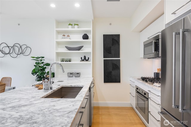 kitchen featuring light stone counters, a sink, light wood-style floors, appliances with stainless steel finishes, and open shelves