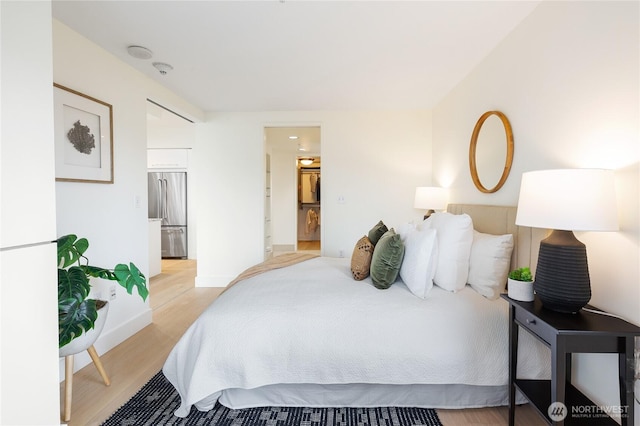 bedroom with light wood finished floors, baseboards, stainless steel refrigerator, and connected bathroom