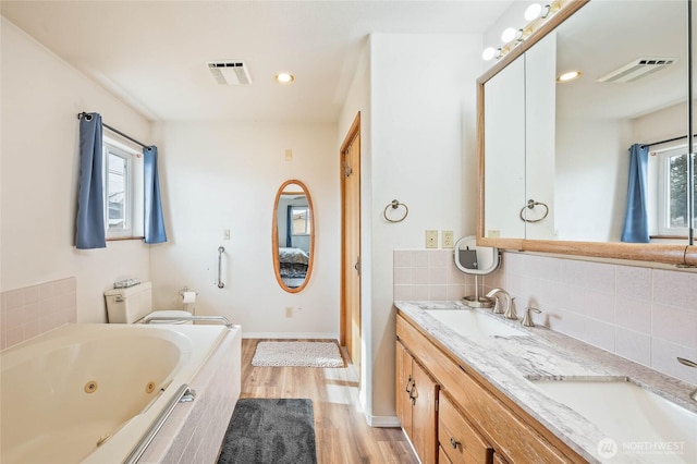 full bathroom with a whirlpool tub, visible vents, backsplash, and a sink