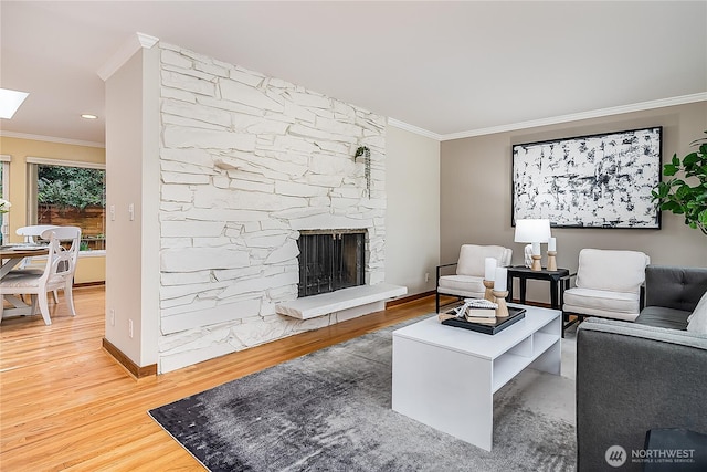 living room with baseboards, ornamental molding, a stone fireplace, a skylight, and wood finished floors