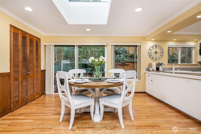 dining space with a skylight, light wood-type flooring, and ornamental molding