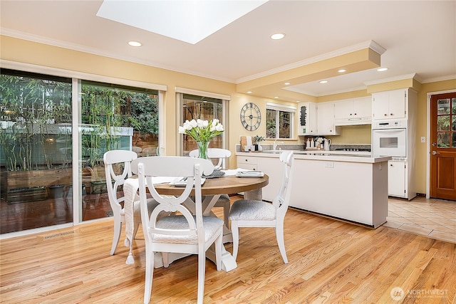 dining area with crown molding, a skylight, recessed lighting, and light wood-type flooring