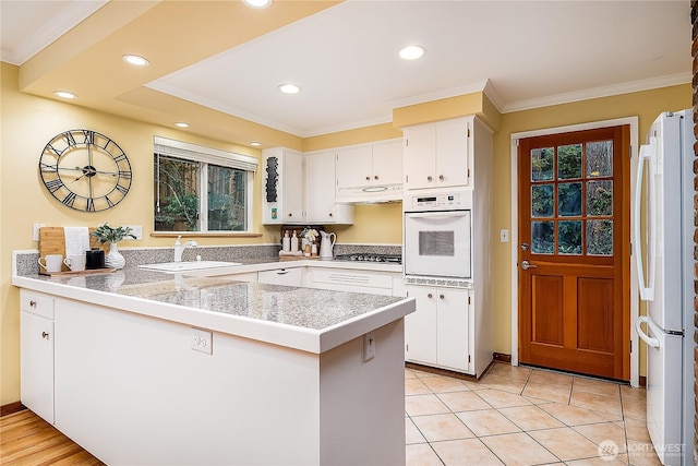 kitchen with white appliances, tile countertops, a peninsula, a sink, and white cabinetry