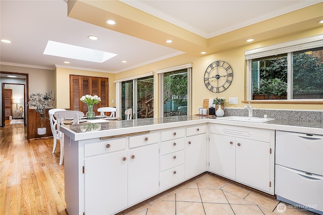 kitchen with a sink, a peninsula, a skylight, and ornamental molding