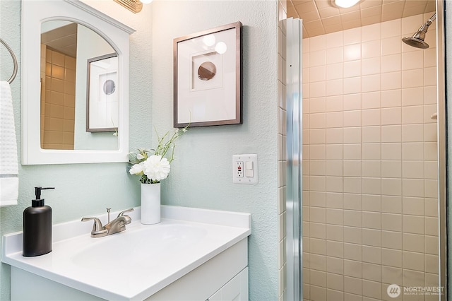 full bathroom with tiled shower, vanity, and a textured wall