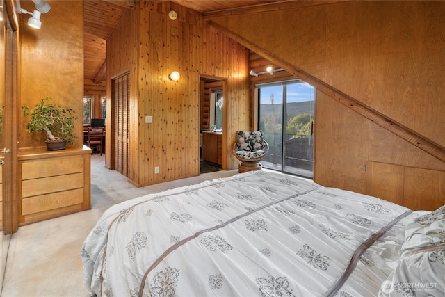 carpeted bedroom with vaulted ceiling, multiple windows, wood walls, and access to exterior