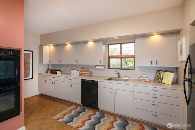 kitchen featuring black appliances, white cabinetry, light countertops, and a sink